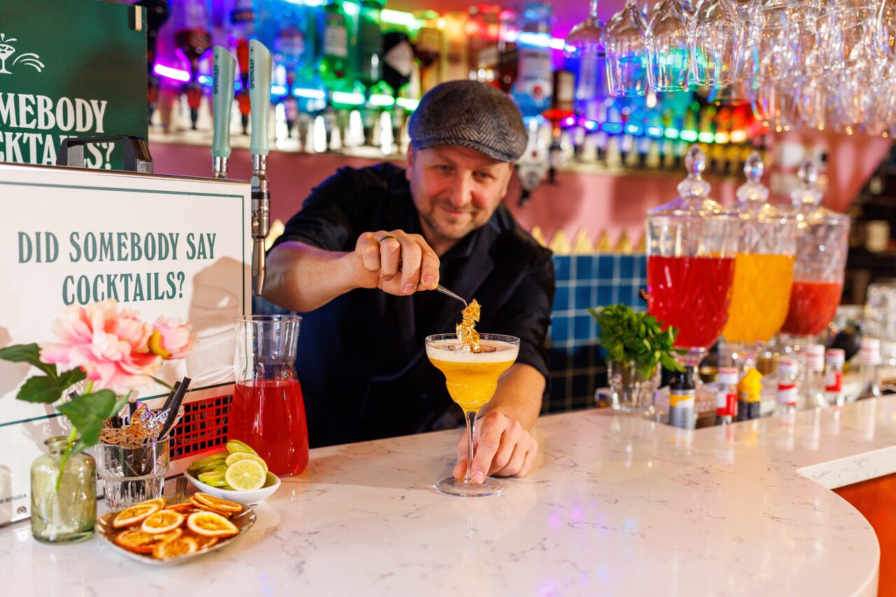 Bartender garnishes a tapped cocktail at a neon-lit bar