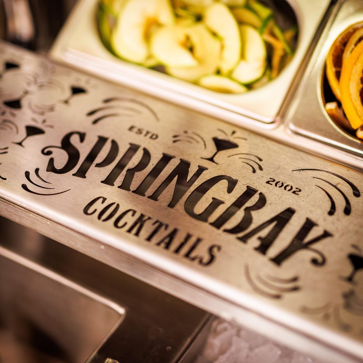 Engraved Springbay Cocktails panel next to the filled garnish trays