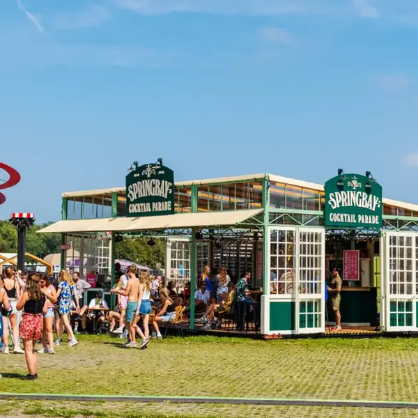 Springbay Cocktail Parade Festivalbar mit grüner Fassade und einer Reihe von Besuchern davor